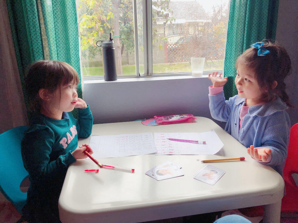 Image of a two preschool girls sitting at a childs table exchanging langauges for dual immersion environment classes