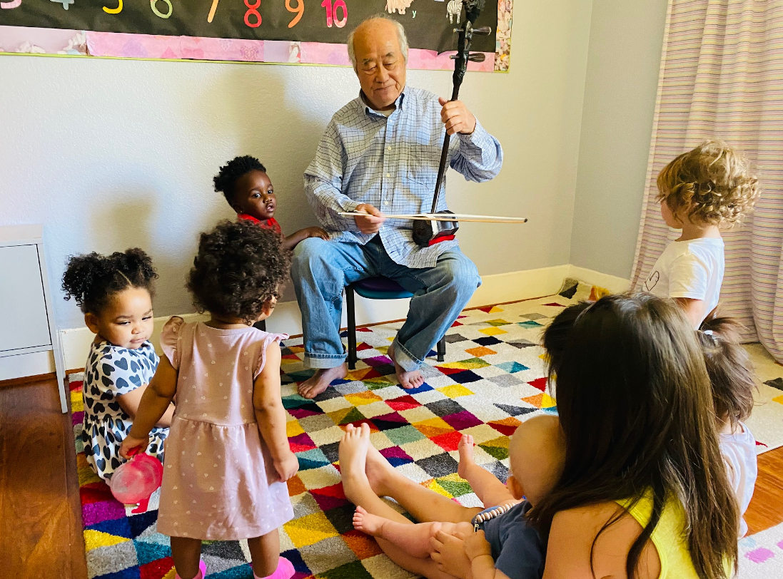 Picture of a group of kids learning music from an elderly man.
